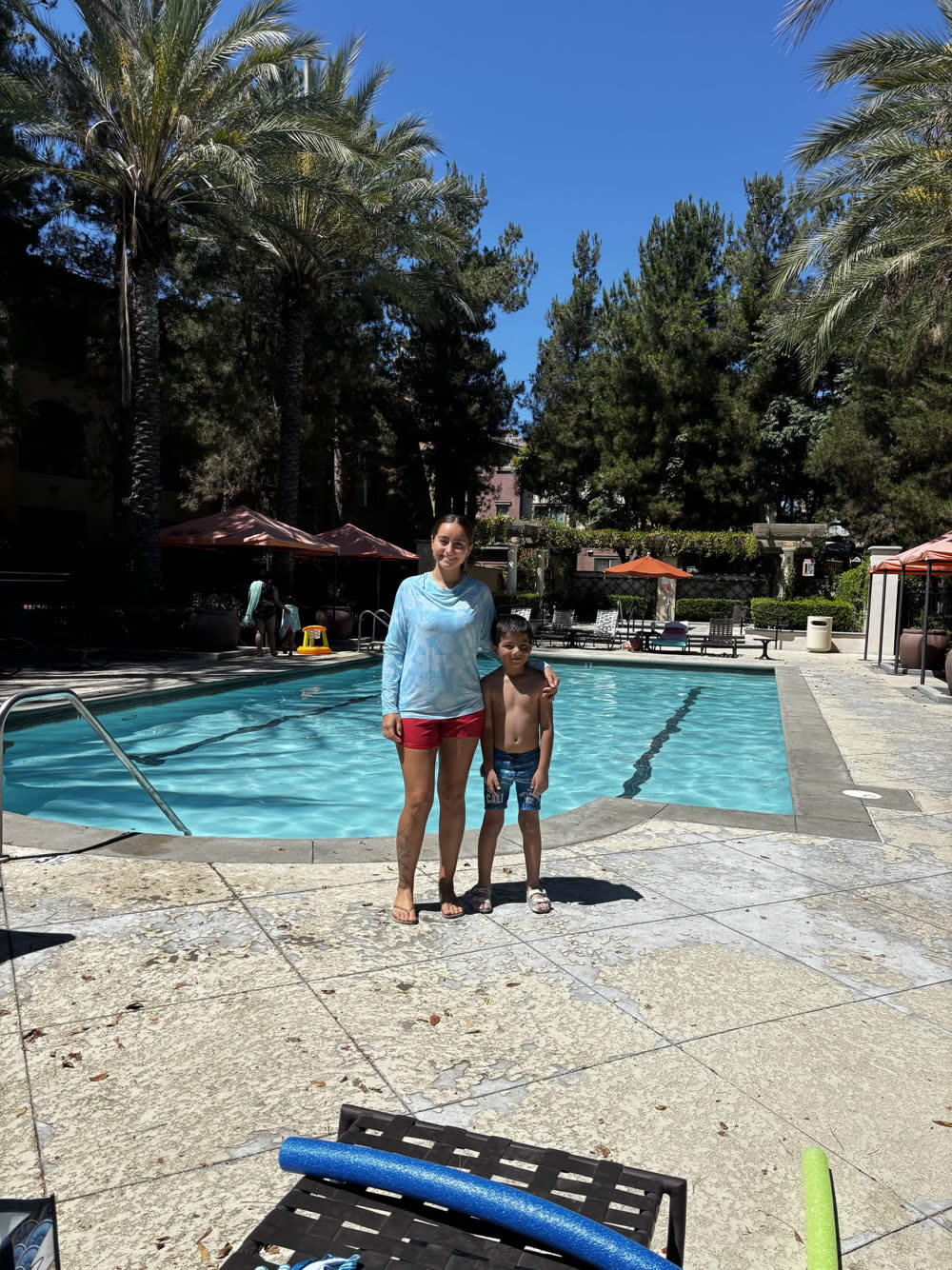 Emmy Catalan standing at the edge of a sunlit pool with one of her young students.
